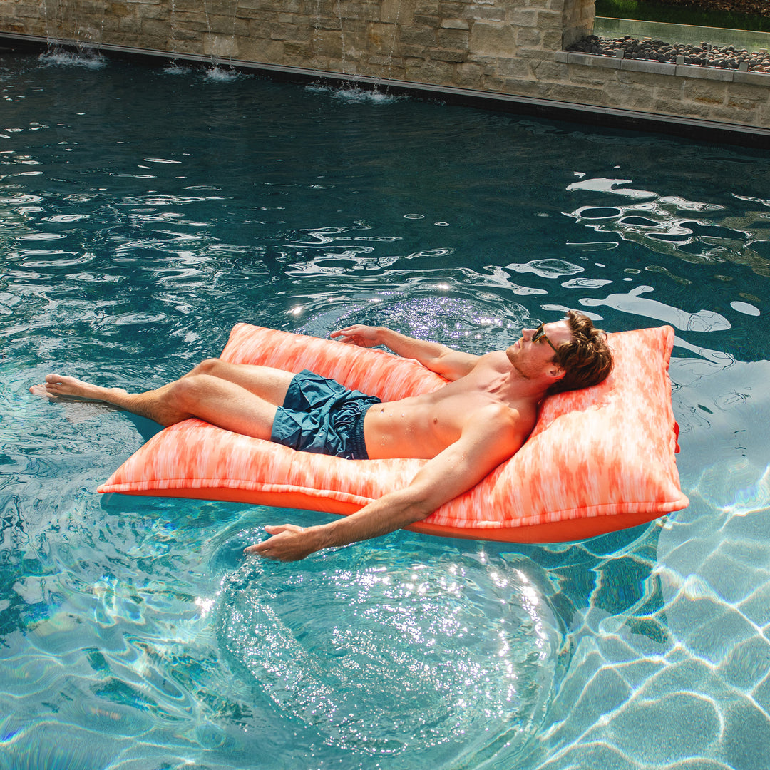 Man lying on a pink pool float in a pool. #color_peach-glow
