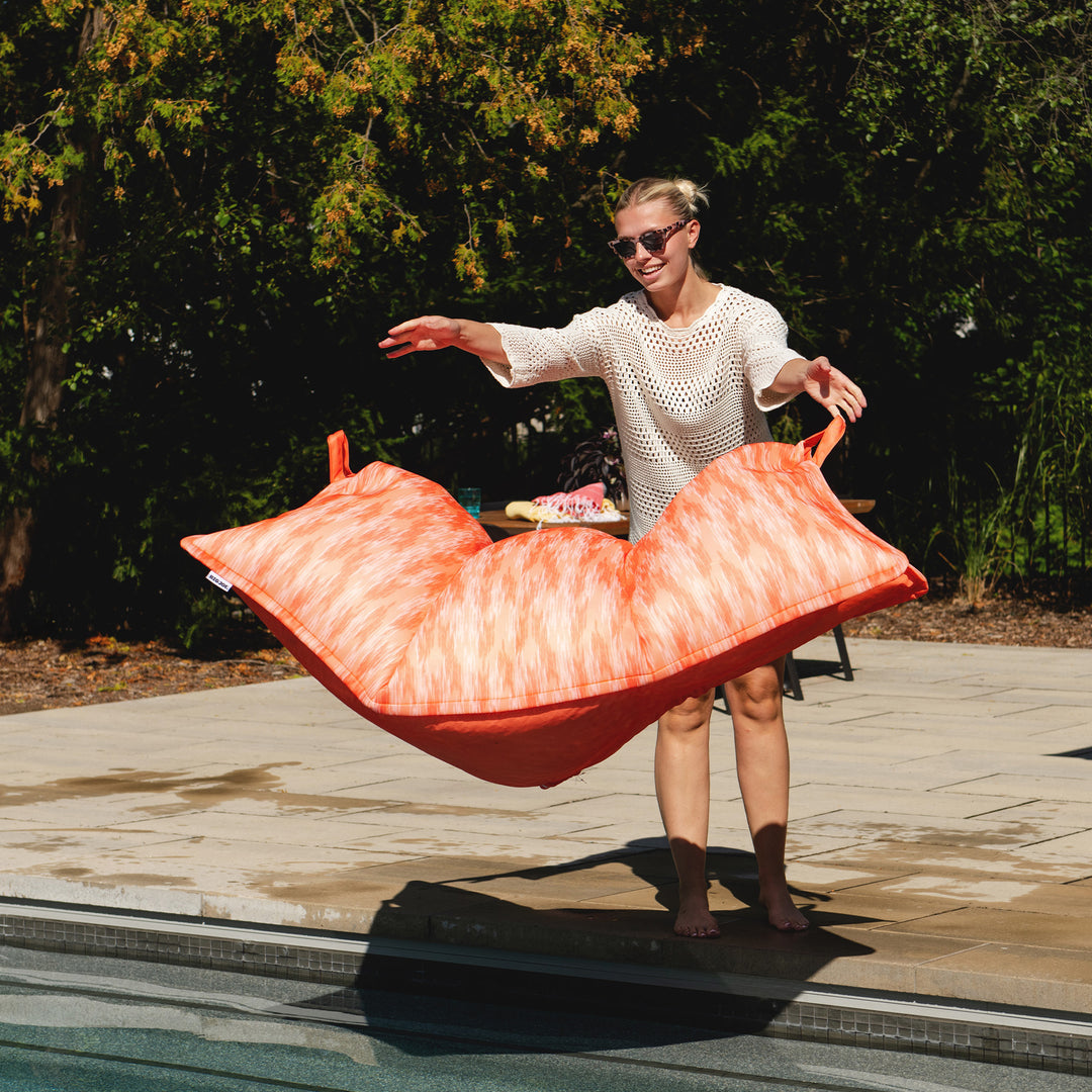 Woman holding a large orange and pink pool toy by a pool #color_peach-glow