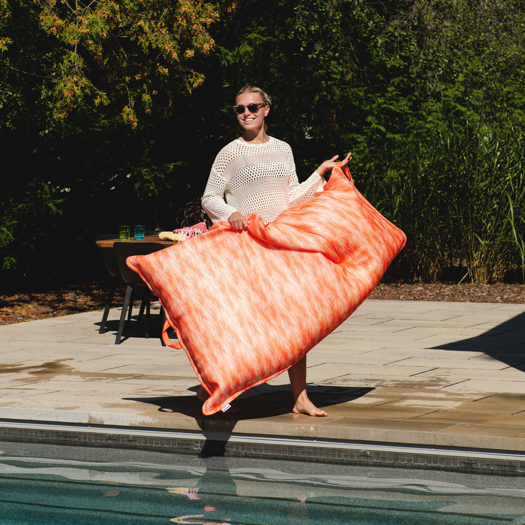 Person holding a large orange mat by a pool #color_peach-glow