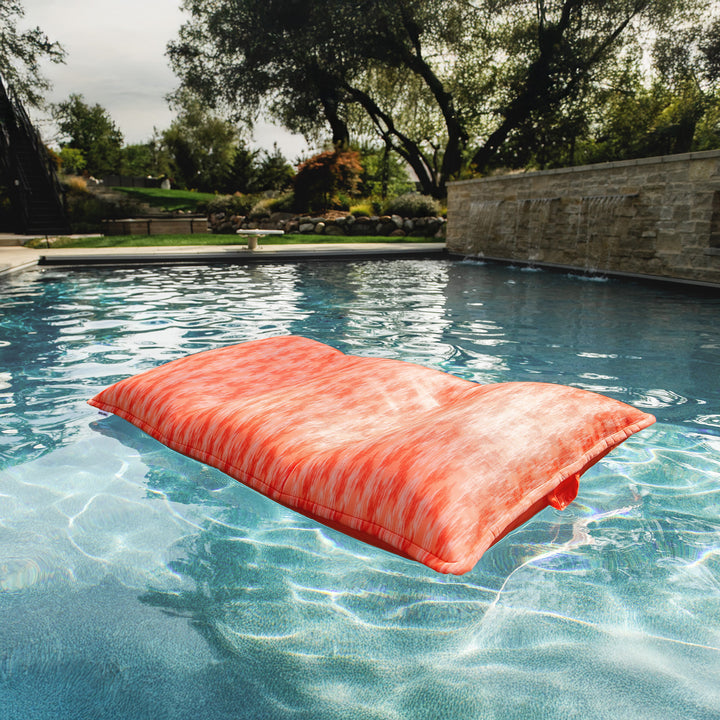 Orange pool float floating in a pool with trees and a stone wall in the background #color_peach-glow