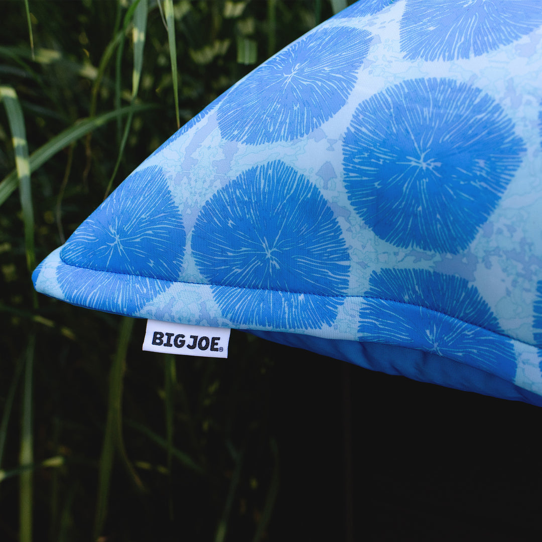 Blue patterned pillow with a visible Big Joe tag against a natural background #color_coral-bloom