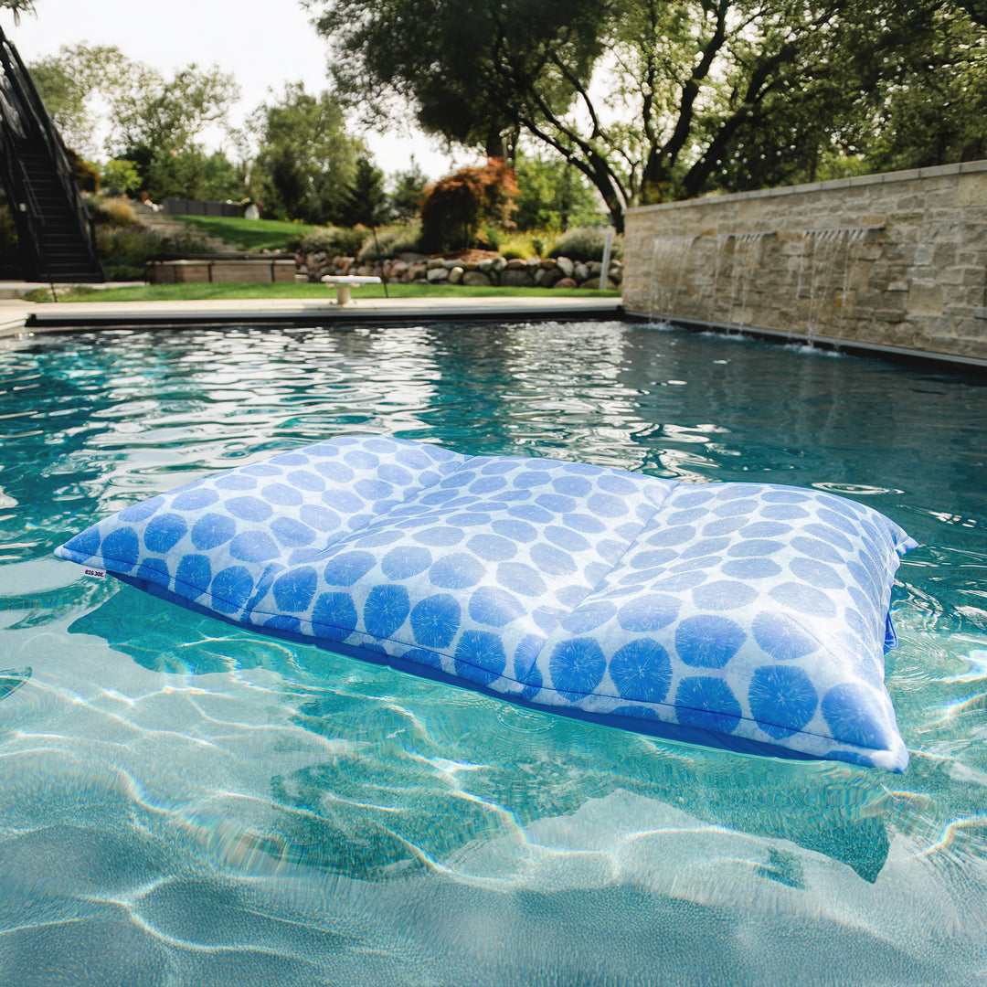 Blue polka dot pillow floating in a pool with a garden and stone wall in the background #color_coral-bloom