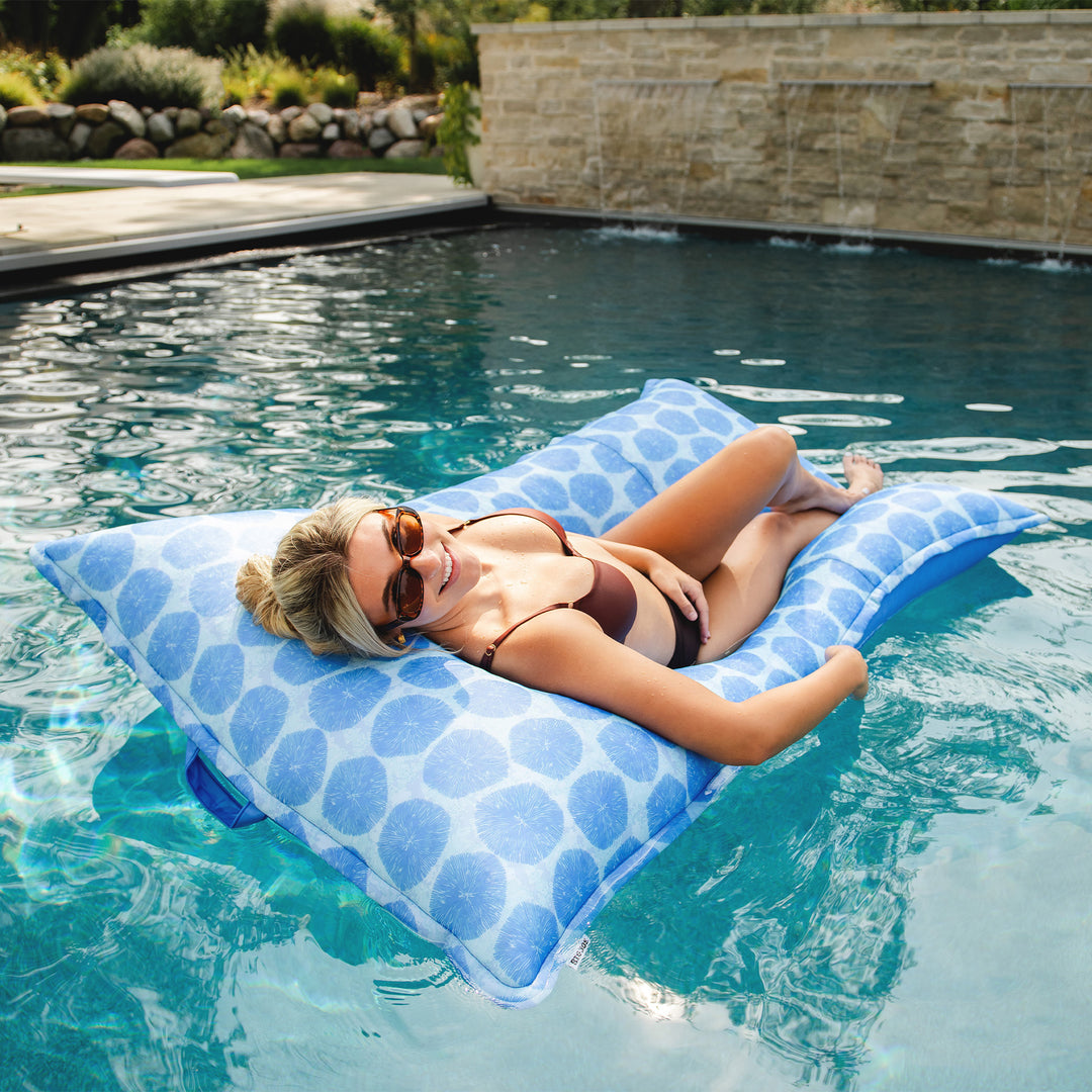 Woman lying on a blue pool pillow by a pool. #color_coral-bloom