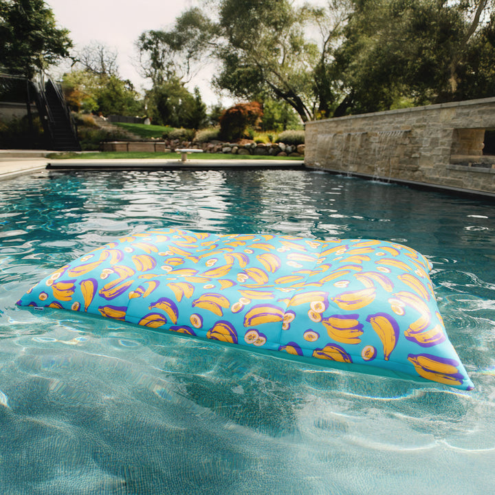 Colorful pool pillow floating in a pool with trees and a stone wall in the background. #color_banana-pop