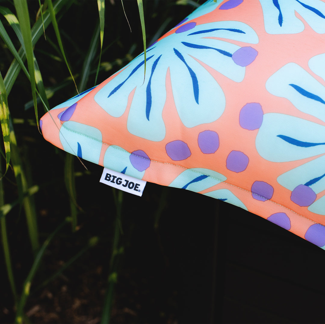 Colorful pillow with leaf pattern and 'BIG JOE' label on grass #color_sweet-shells-peach