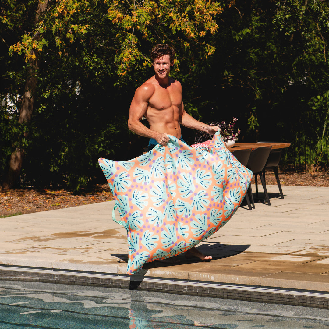 Man holding a colorful pool lounger by a poolside #color_sweet-shells-peach