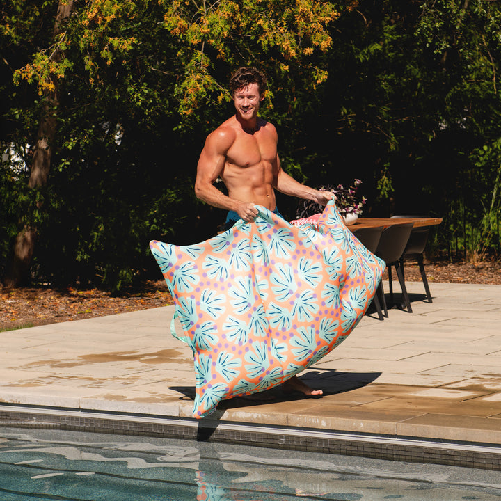 Man holding a colorful pool lounger by a poolside #color_sweet-shells-peach