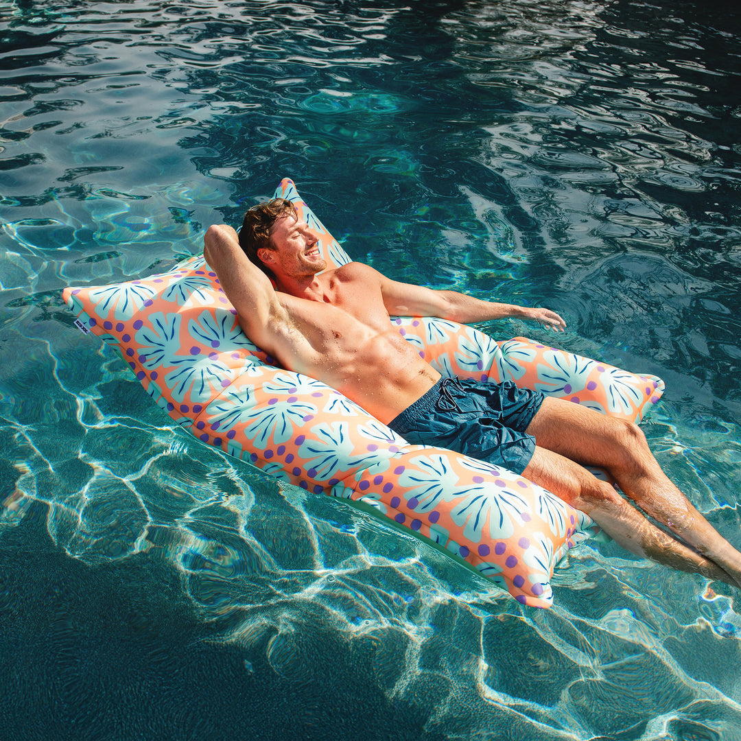 Man lying on a colorful pool float in clear blue water #color_sweet-shells-peach
