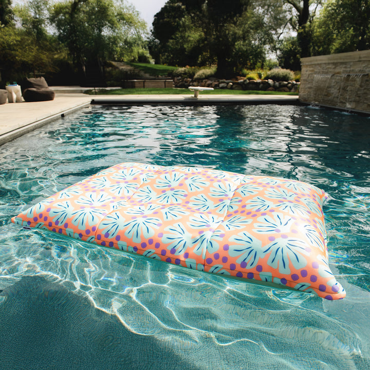 Colorful water pillow floating in a pool with trees and garden in the background #color_sweet-shells-peach