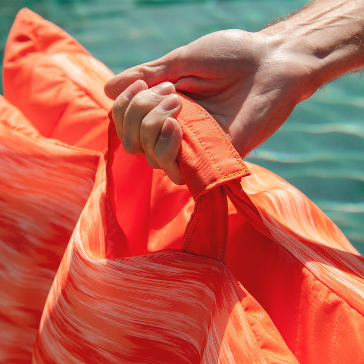 Close-up of a person holding an orange pool float with water in the background #color_peach-glow
