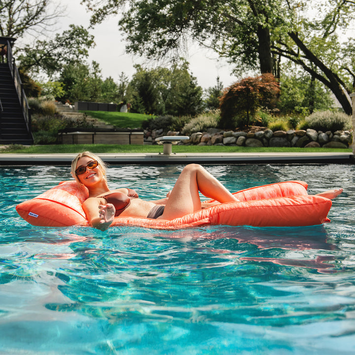 Woman relaxing on an orange pool float in a pool with trees and greenery in the background #color_peach-glow