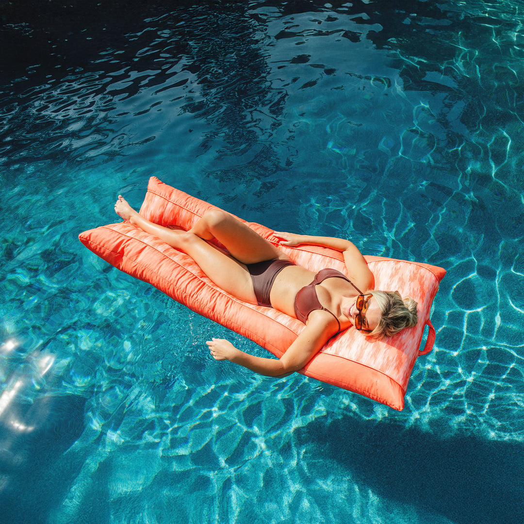 Woman relaxing on a pink raft in clear blue water #color_peach-glow