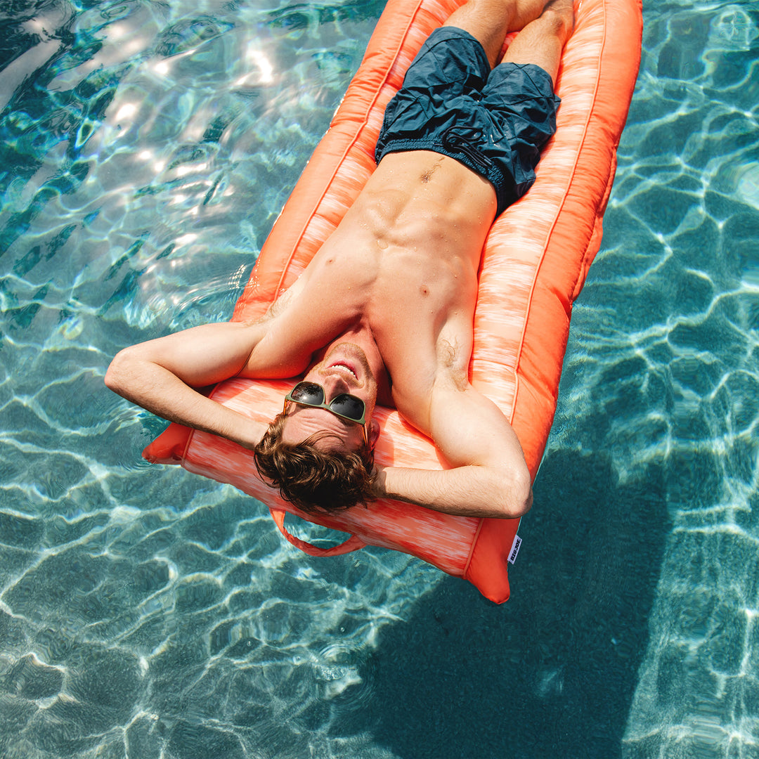 Person lying on an orange raft in a pool #color_peach-glow