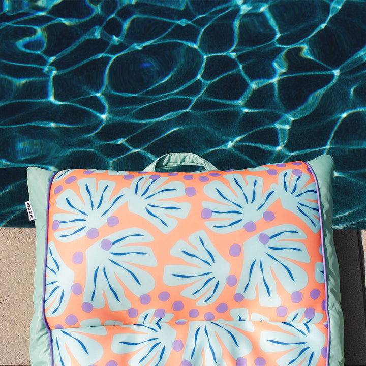 Colorful floral-patterned towel on a chair by a pool #color_sweet-shells-peach