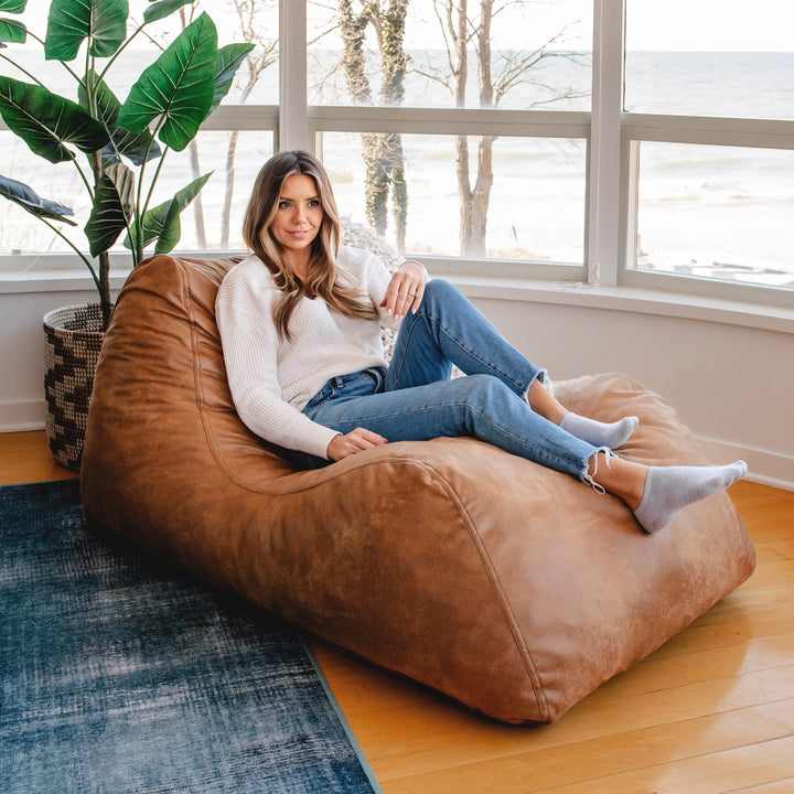 Woman relaxing on the Delmont Chaise Lounger #color_vintage-brown-vegan-suede