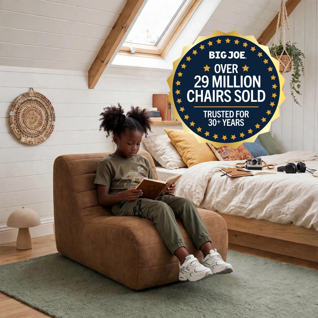 A child sits in a brown upholstered armchair reading in a bright bedroom with white wood walls, a bed, skylight, and green rug. A large circular badge reads &