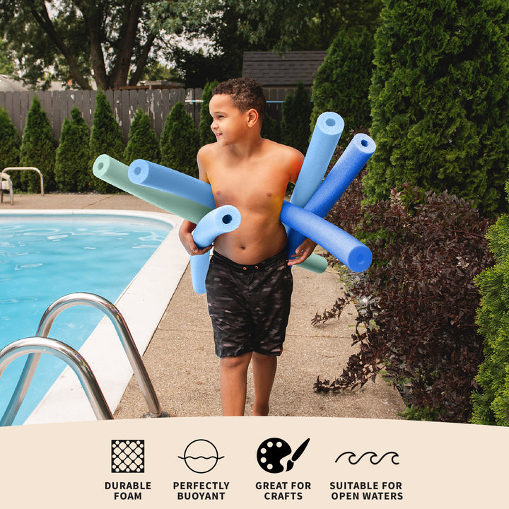 A young boy stands beside a swimming pool holding a bundle of blue and light blue foam pool noodles. The photo is taken outdoors in a backyard with trees, shrubs, and pool railings visible. 