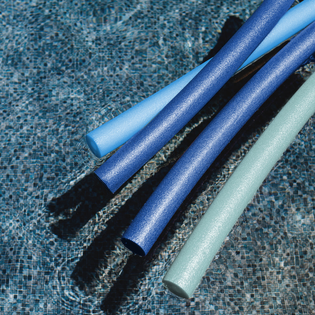 Three pool noodles in blue and mint green resting on a tiled swimming pool floor. 