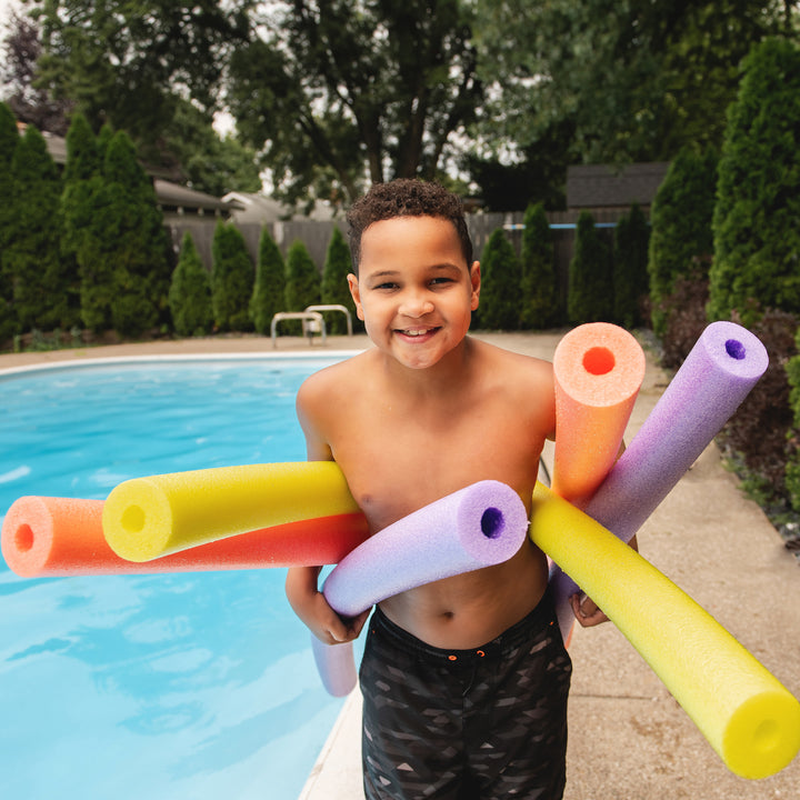 Child holding colorful pool noodles by a pool 