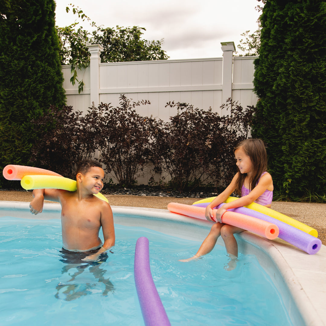 Two children playing with pool noodles in a backyard pool. 