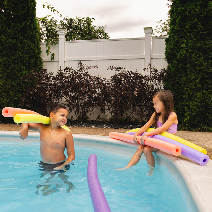 Two children playing with pool noodles in a backyard pool. 