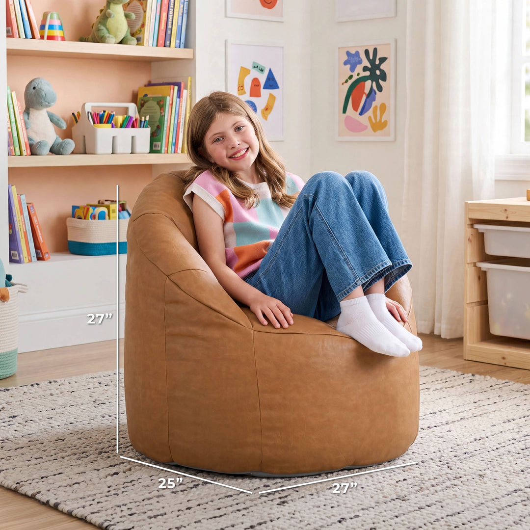 A child sits on a large tan bean bag chair in a bright playroom. White dimension lines on the image show the chair&