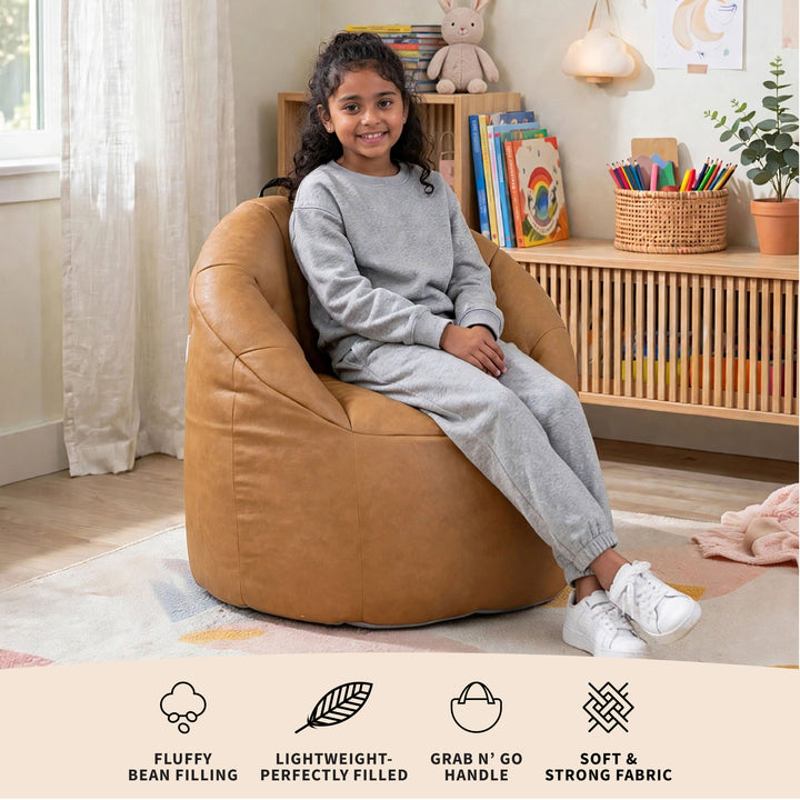 A child wearing a gray sweatshirt and matching sweatpants sits in a tan leather bean bag chair in a bright, modern children&