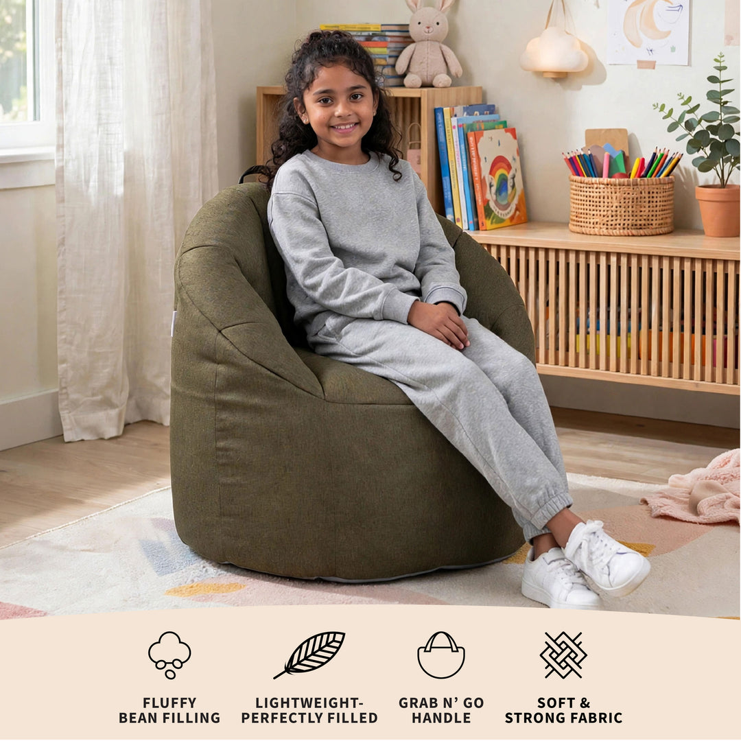 A child wearing a gray sweatshirt and matching sweatpants sits on a large olive green bean bag chair in a bright, modern children&