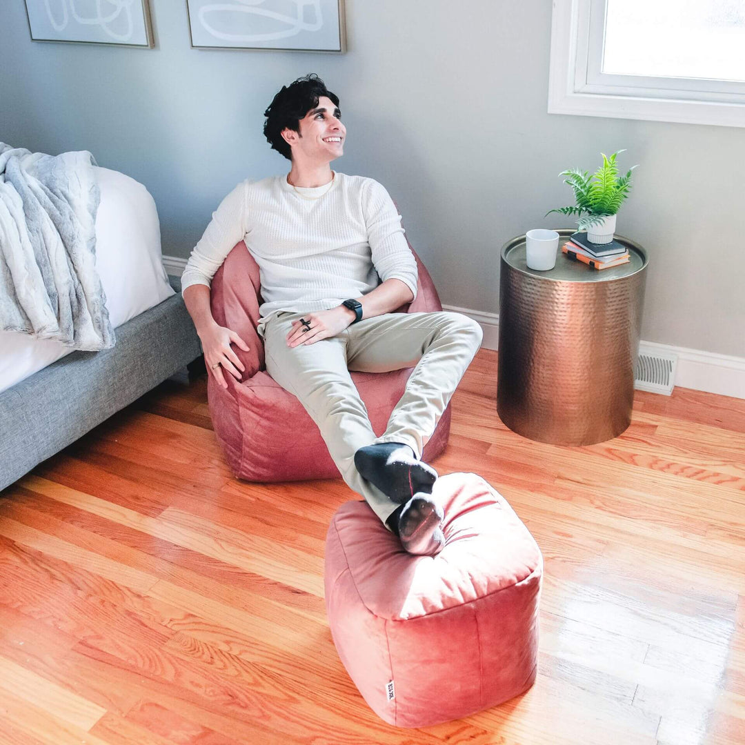 Man sitting on bean bag chair in room with ottoman #color_toasted-mauve-velvet