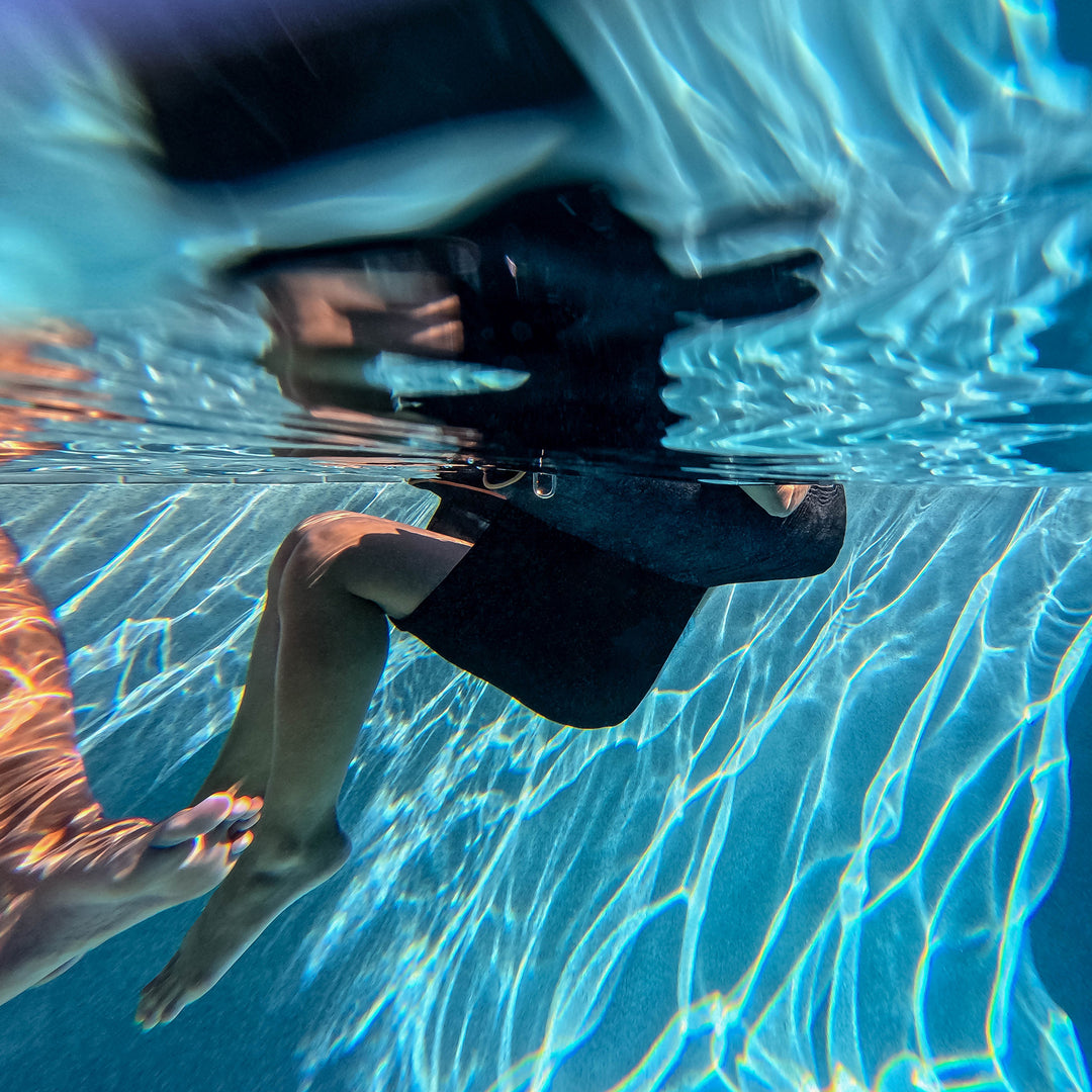Person floating from under water view on the Bali Sling Pool Float #color_twilight-sunbrella-fabric