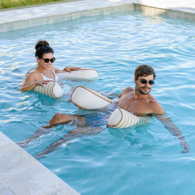 Two people in a pool with white sling chair floats. 
