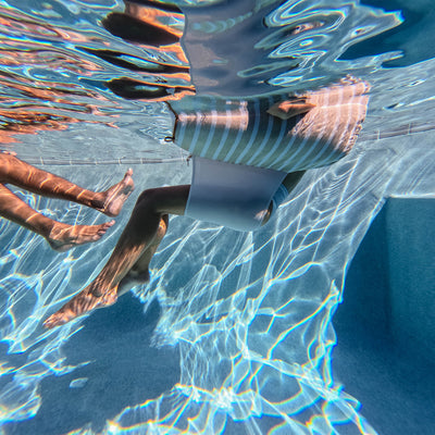 Person floating underwater with clear blue water on a sling chair float  