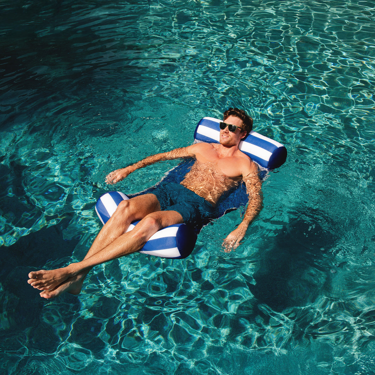 Man lounging on a striped pool float in clear blue water 
