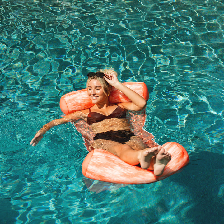 Woman relaxing on a pink flamingo pool float in clear blue water #color_peach-glow
