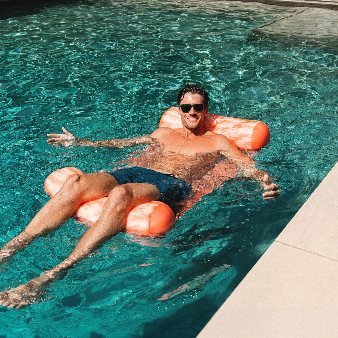 Man floating on an orange noodle sling in a pool #color_peach-glow