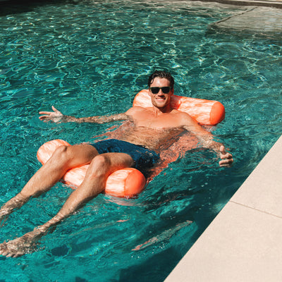 Man floating on an orange noodle sling in a pool 