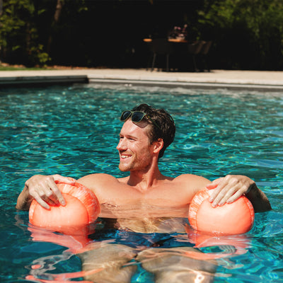 Man floating in a pool with two pink bouys 