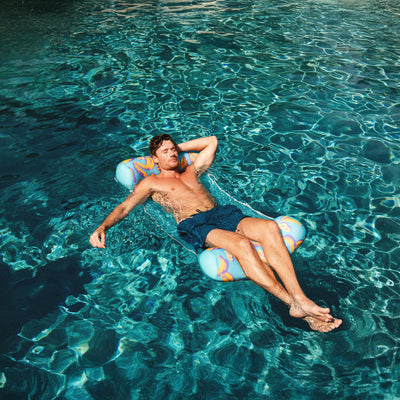 Man relaxing on a colorful pool hammock in clear blue water 