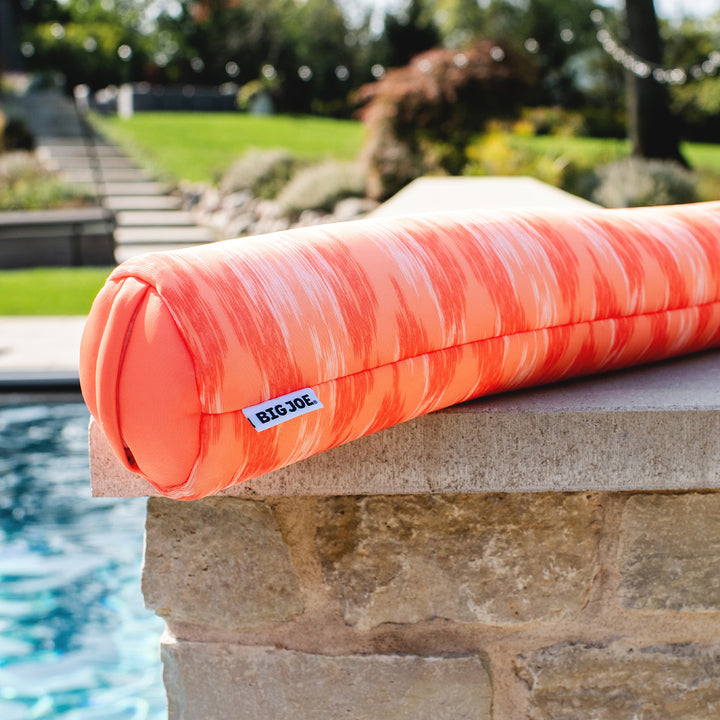 Orange striped pool noodles on a stone ledge by a pool with a garden background #color_peach-glow