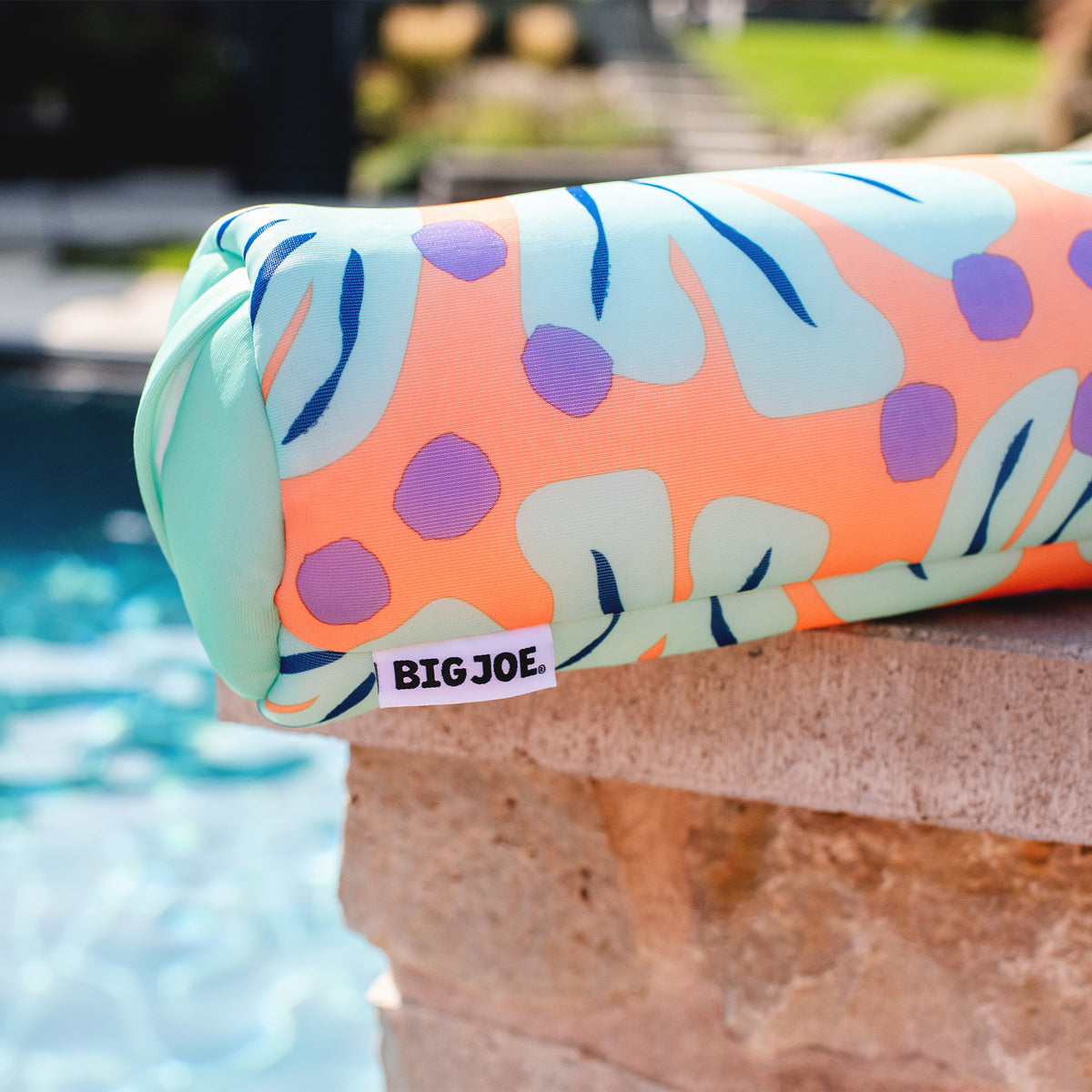 Colorful pool floatie with leaf pattern on a poolside ledge, featuring the brand 'BIGJOE'. 