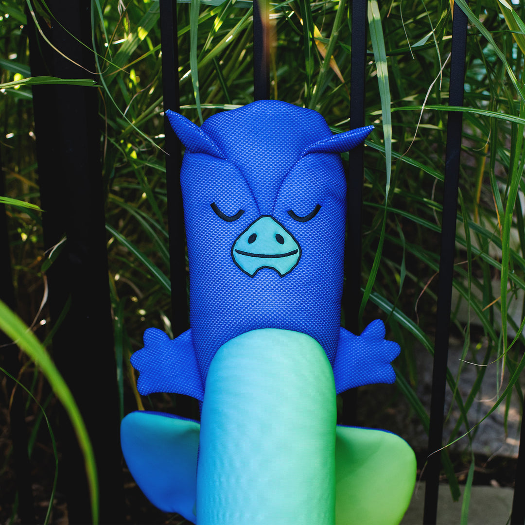 Blue and green plush toy with a face design held by a hand against a natural background #style_dragon