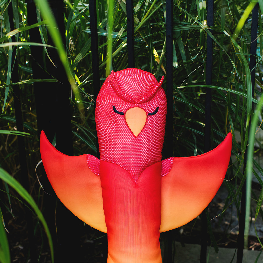 Red and orange bird-shaped pool toy float against a green leafy background #style_phoenix