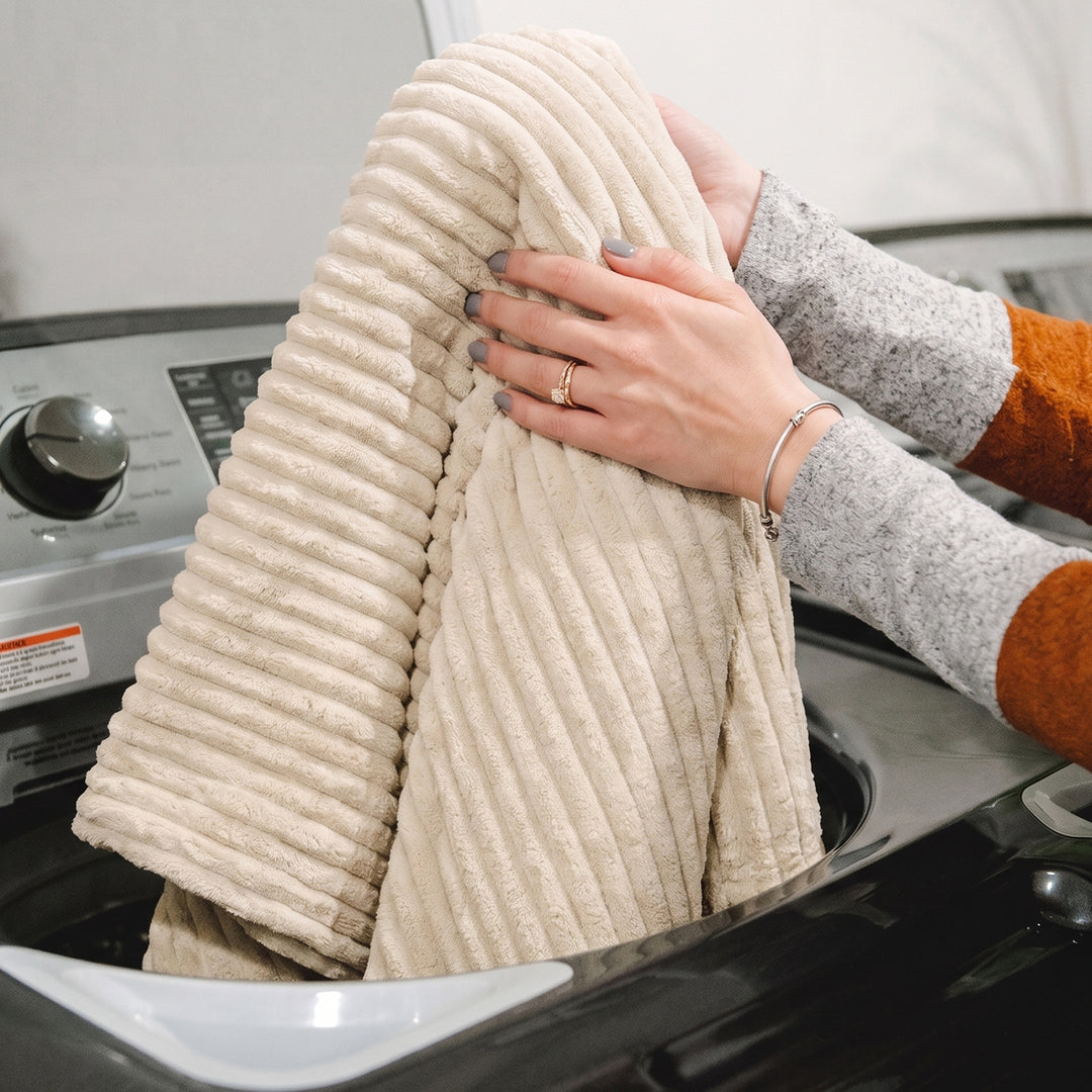 A person holding a folded ribbed cream corduroy blanket or towel over a washing machine. 