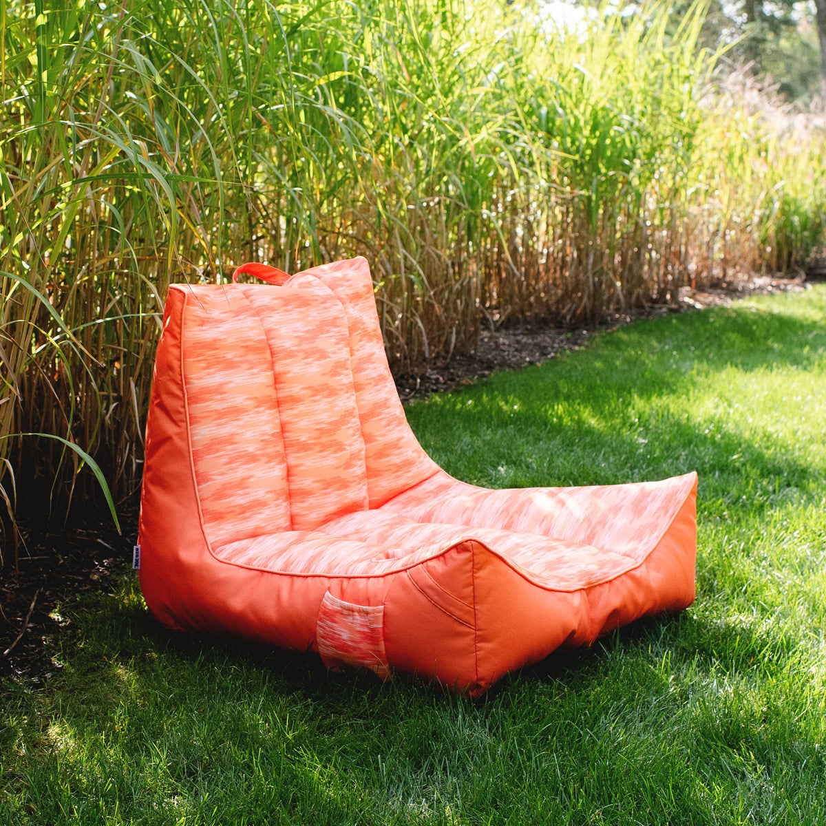 Orange bean bag chair on grass with tall grasses in the background 