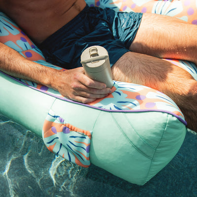 Person lying on a colorful pool float holding a beige water bottle. 
