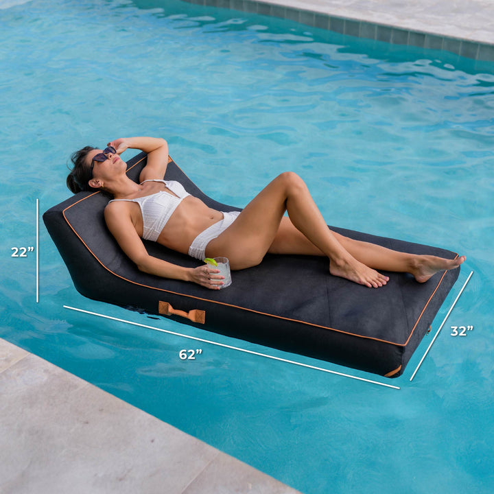 Woman lying on a black pool float with measurements, by a pool. #color_twilight-sunbrella-fabric