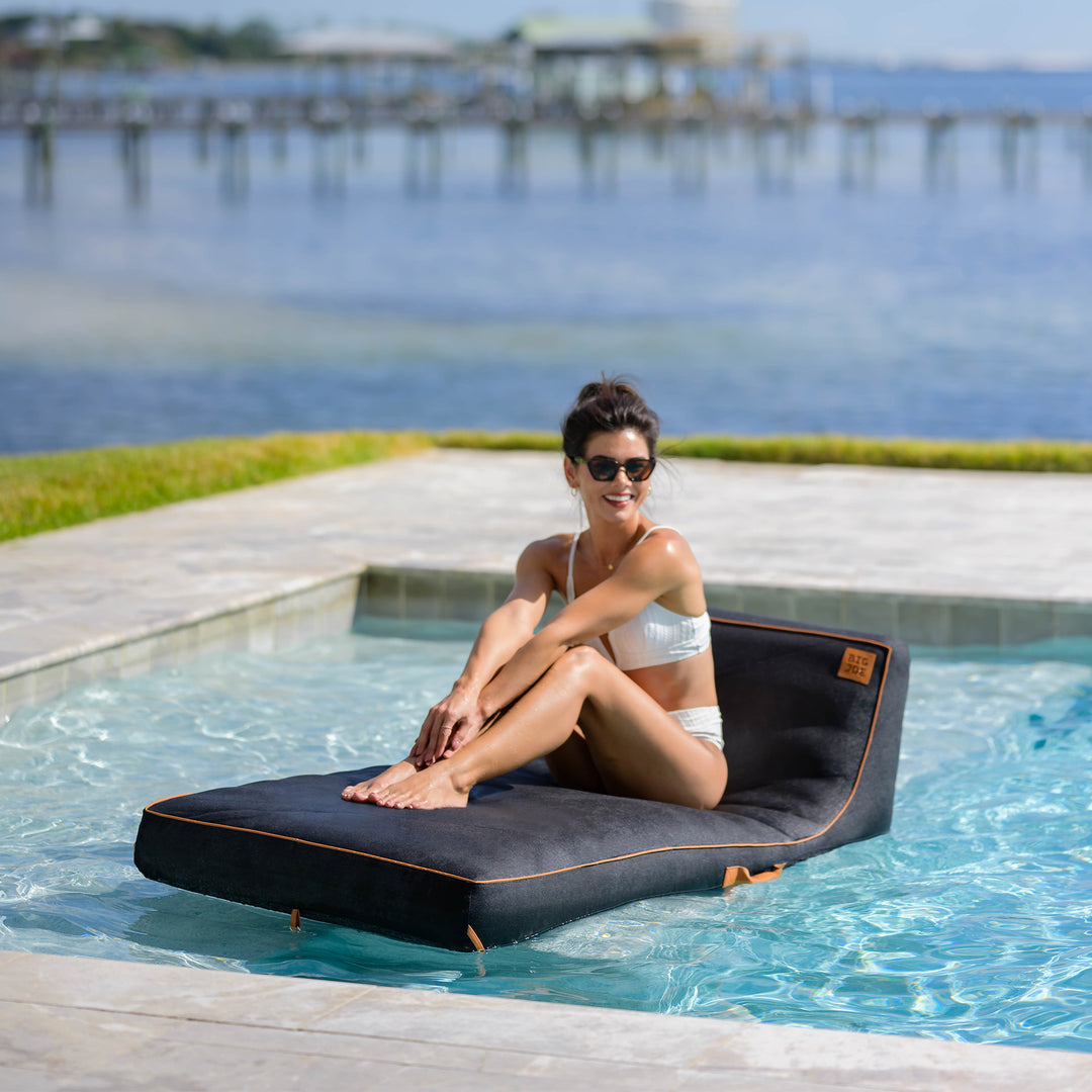 Woman sitting on a floating lounge by a pool with a scenic background #color_twilight-sunbrella-fabric