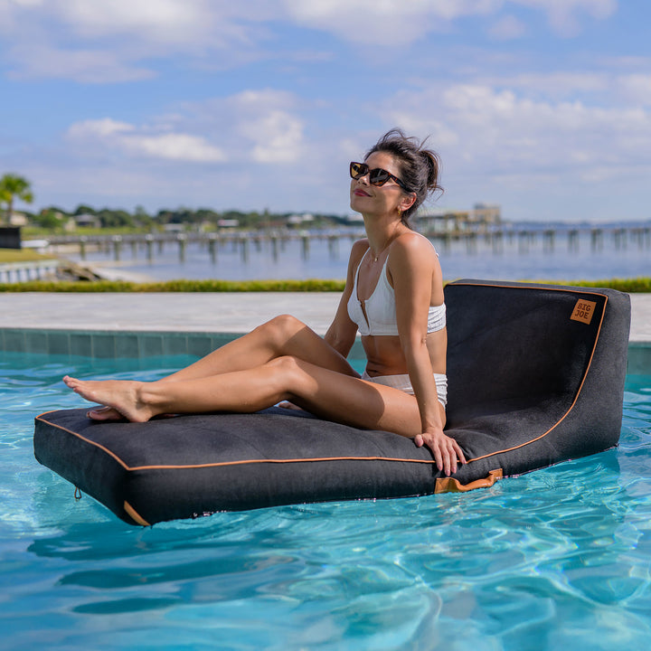 Woman relaxing on a floating inflatable lounger in a pool with a scenic background. #color_twilight-sunbrella-fabric