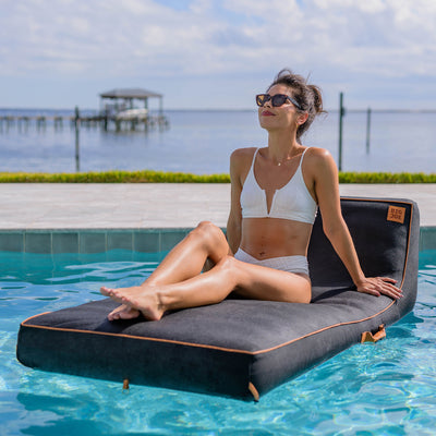 Woman sitting on a floating platform by a pool with a scenic background 