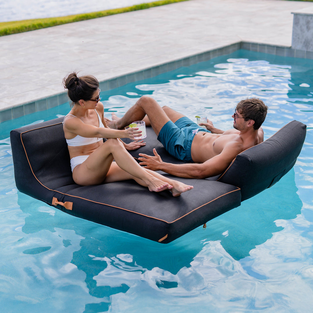 Two people relaxing on a floating lounge in a pool #color_twilight-sunbrella-fabric